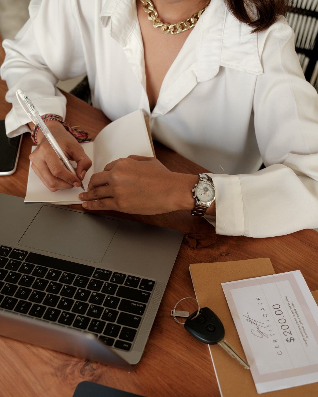Mãos de uma profissional fazendo anotações em um caderno ao lado do notebook